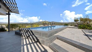 Une piscine sur le toit offrant une vue sur les montagnes lointaines, entourée d’une terrasse avec des marches et du mobilier d’extérieur.