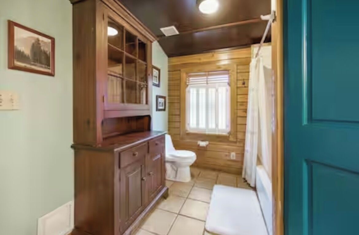 A bathroom with a wooden vanity, a toilet, and a window with curtains.