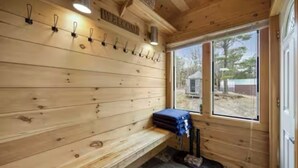 Un intérieur en bois avec un banc, un porte-manteau fixé au mur et une fenêtre donnant sur les arbres.