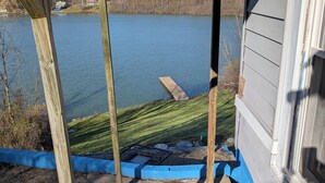 A wooden deck with a view of a lake and a house in the background. - Lakefront Haven w/ 50-ft Dock 4BR Near Punderson Park & Amish Country EV Charger (Newbury)
