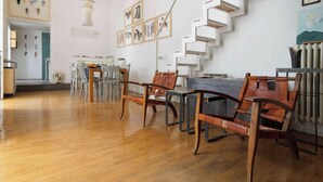 Una habitación amplia con piso de madera, un comedor con sillas y una mesa, una escalera blanca y obras de arte en las paredes.