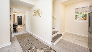 Un interior moderno con un pasillo que conduce a una escalera, un tapete estampado y un aplique de pared.