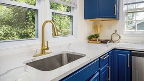 Una cocina con encimera de mármol blanco, grifo dorado y armarios azules.