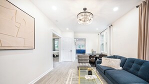 Una sala moderna con un sofá azul, una mesa de centro de cristal y una araña.