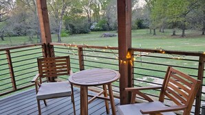 Une terrasse en bois avec une table et des chaises, entourée d’une rambarde et illuminée de guirlandes lumineuses.
