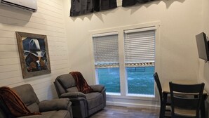 Une pièce comprenant deux fauteuils inclinables, une table à manger en bois avec une chaise, et une grande fenêtre avec des stores.