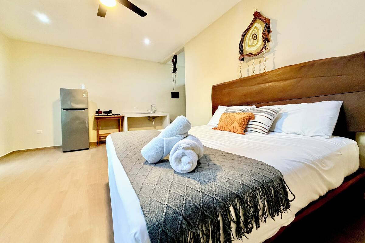 Habitación de hotel con cama, escritorio, refrigerador y ventilador de techo.