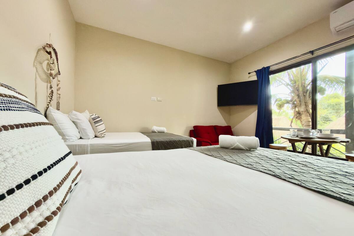Una habitación de hotel con una cama grande, un sofá, una mesita con una taza y un plato, y un televisor colgado en la pared.