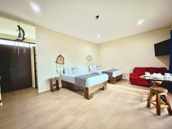 A hotel room with two beds, a red sofa, a small table with a chair, and a wall-mounted TV. - Casa Nohoch Tunich (Tulum)