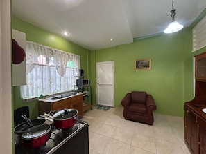 A compact kitchen with a stove, pots, a microwave, and a sink. There is a brown chair and a door in the room.