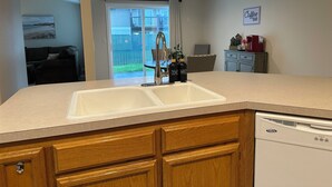 A kitchen with a double sink, wooden cabinets, a dishwasher, and a dining area with a table and chairs. - Kozy Keizer Getaway with Fireplace (Keizer)