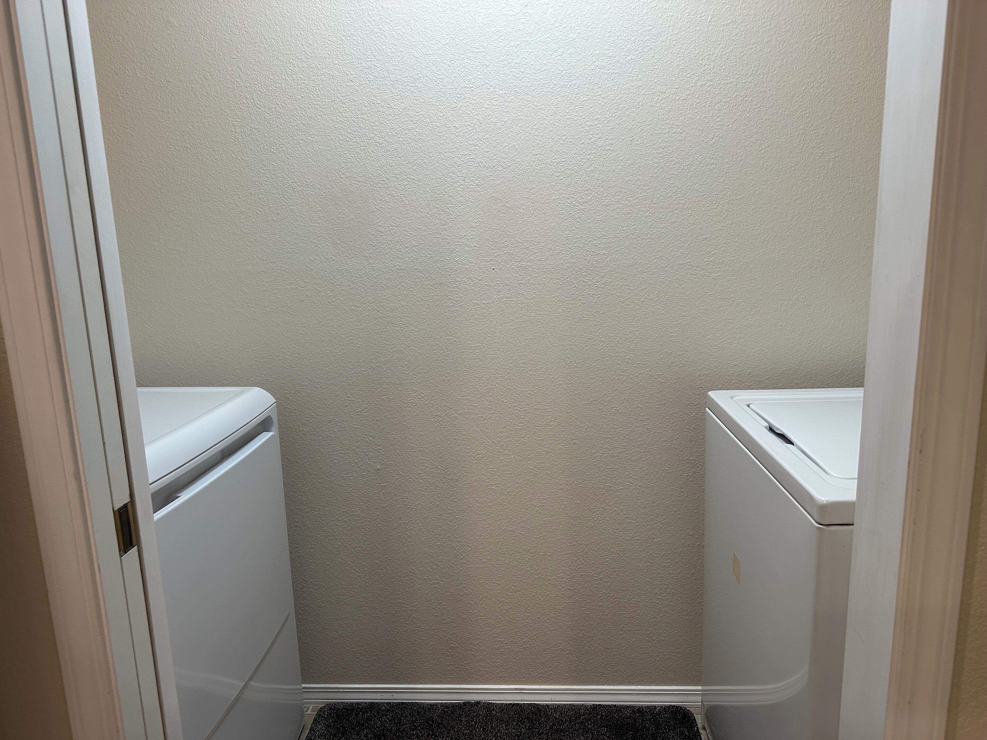 A small, enclosed bathroom with two white toilets and a black doormat at the entrance.