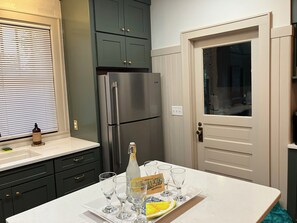 A kitchen with a stainless steel refrigerator, dark green cabinets, a white countertop, and a door with a window.
