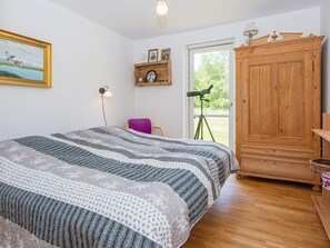 A bedroom with a large bed, a wooden wardrobe, a desk with a lamp, a chair, a telescope, and a window with a view of greenery. - 5 Star Holiday Home in Engesvang (Engesvang)
