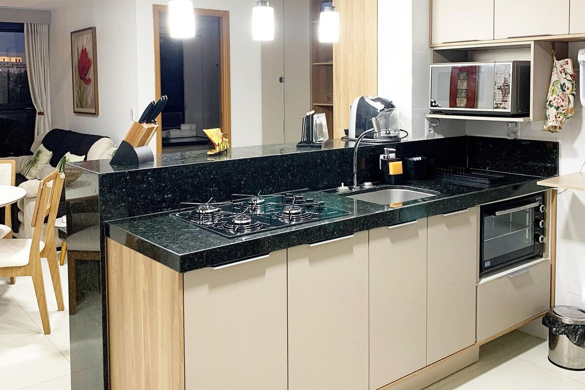 Una cocina moderna con una isla central, electrodomésticos integrados, iluminación colgante y un comedor con sillas y una mesa.