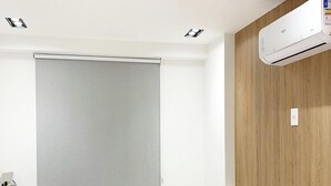 A hotel room with a bed, a window with a blind, an air conditioning unit, and a wooden accent wall. - Dutra Ocean Flat By DayByDay (Joao Pessoa)