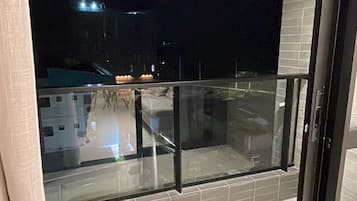 Varanda com porta de vidro, chão de azulejos e vista para um edifício à noite.