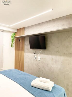 A modern hotel room with a bed, a mounted TV, and a wall-mounted power outlet. - Dutra Ocean Flat By DayByDay (Joao Pessoa)