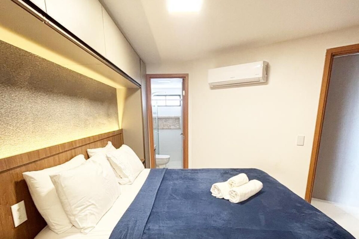 Habitación de hotel con cama, mesita de noche, una silla y un baño visible a través de una puerta abierta.