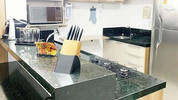 A kitchen with a central island, a microwave, a refrigerator, and hanging kitchen utensils.