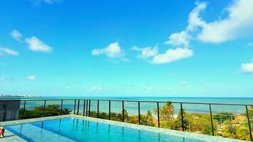 Céu azul e límpido com piscina e vista para o oceano.