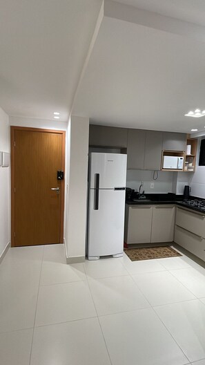A modern kitchen with white cabinets, a white refrigerator, a microwave, and a black countertop. - Dutra Ocean Flat By DayByDay (Joao Pessoa)