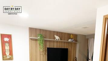 A modern living room with a dining area, a flat-screen TV mounted on the wall, and a small round table with a plant.