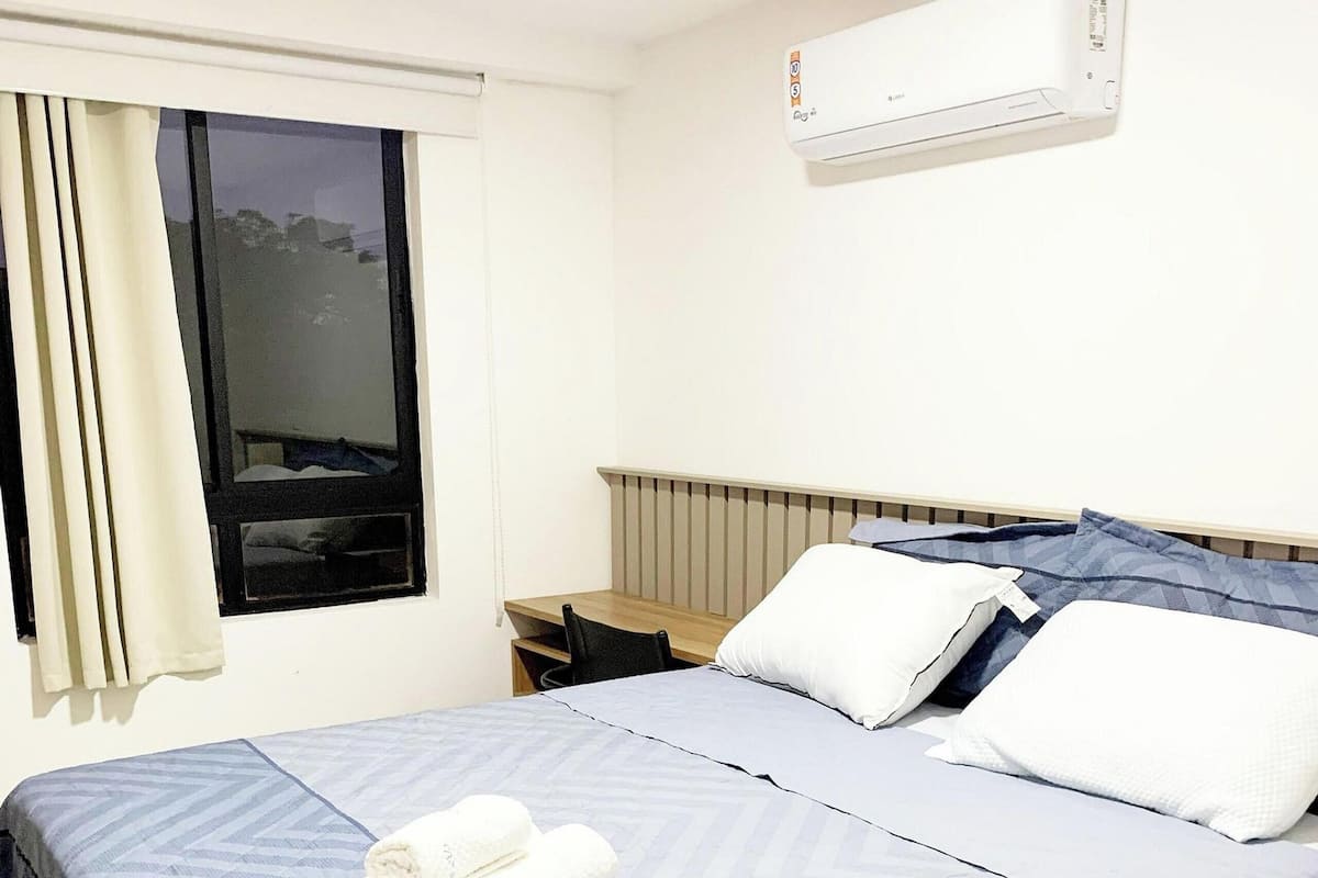 Una cama bien hecha con una colcha azul y blanca estampada, un cabecero de madera y una ventana con cortinas.