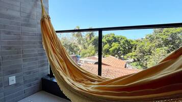 A hammock on a balcony with a clear view of a red-tiled roof and greenery in the background.