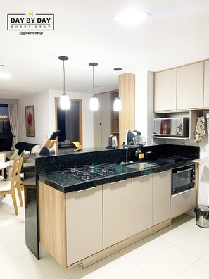 A modern kitchen with a central island, built-in appliances, pendant lighting, and a dining area with chairs and a table.