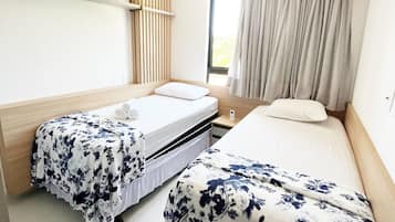 A hotel room with two beds, a window with curtains, a wall-mounted air conditioner, and a wooden panel on the left wall.