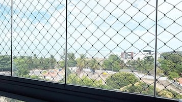 A view through a window with a chain-link fence, featuring a residential area with houses and greenery.