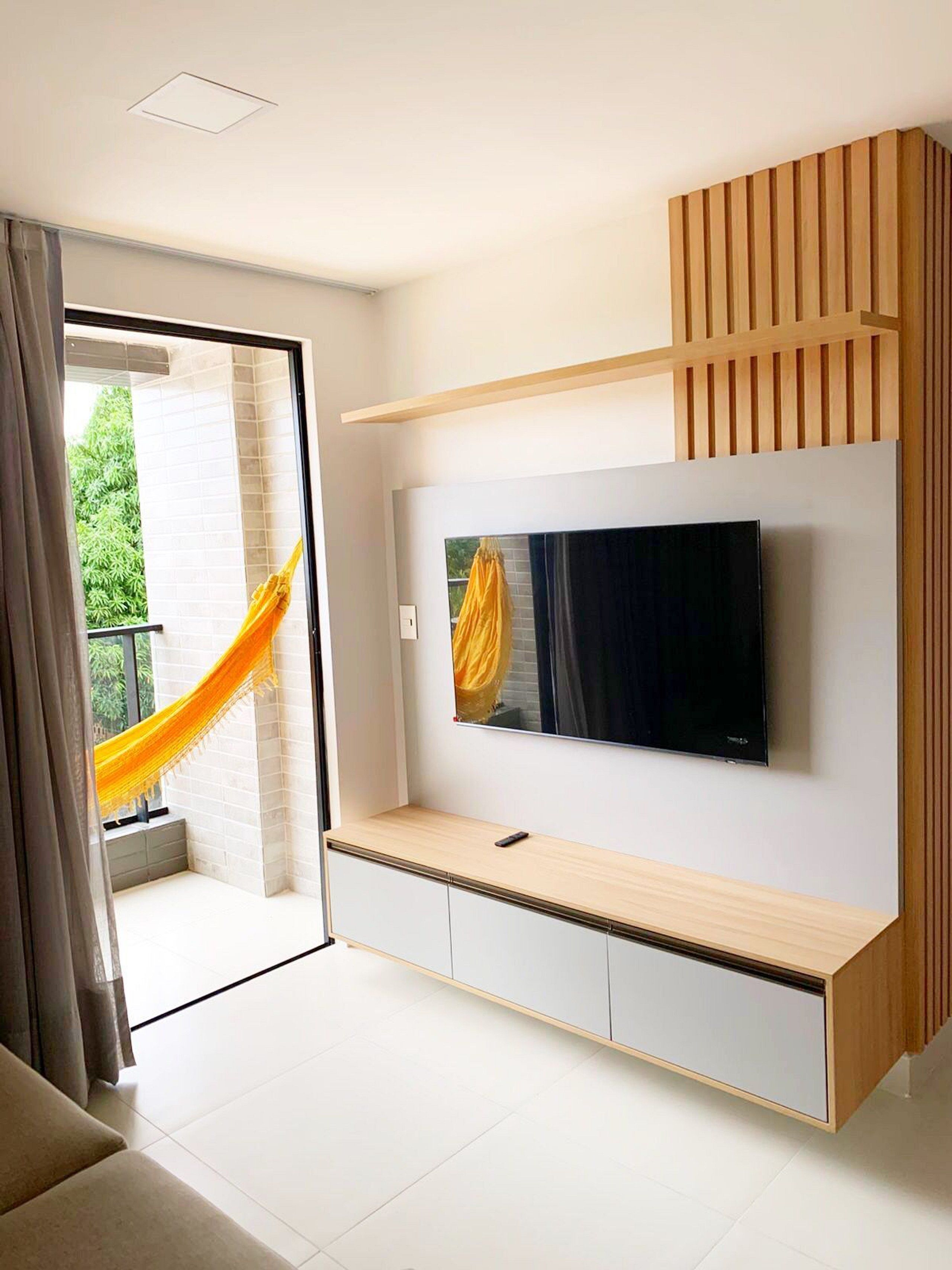 Un salon moderne avec un téléviseur à écran plat fixé au mur, un meuble télé en bois et un hamac près de la porte-fenêtre coulissante.