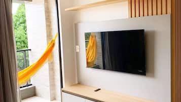 Un salon moderne avec un téléviseur à écran plat fixé au mur, un meuble télé en bois et un hamac près de la porte-fenêtre coulissante.
