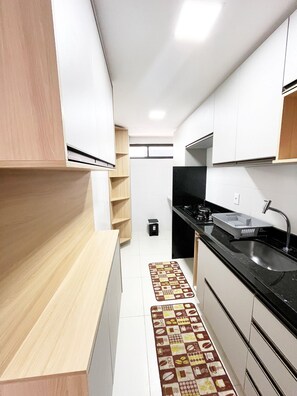 Una cocina moderna con armarios blancos, encimera negra y alfombra estampada.