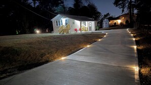 Un sendero de concreto con luces colgantes que lleva a una casa con porche y garaje.