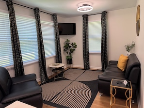 A modern living room with a black sofa, a round coffee table, a small side table, and a large potted plant.