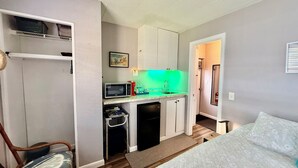 A compact room with a kitchenette, a bed, and a chair.