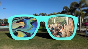 A pair of turquoise sunglasses with a colorful abstract design on the lenses and a photograph of an owl on the frame.