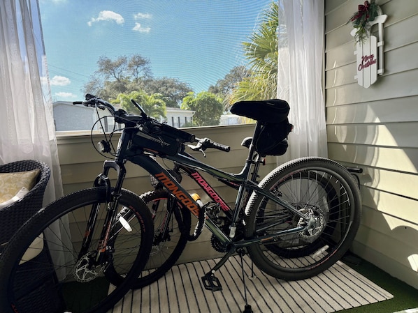 Un vélo est garé sur un porche, avec vue sur des arbres et une maison en arrière-plan.