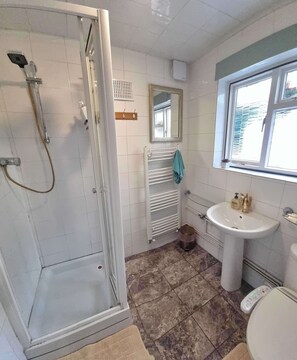 Une salle de bain avec une douche, un lavabo, un miroir et une fenêtre.