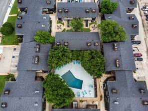 An aerial view of a residential complex with multiple apartment buildings, a central swimming pool, and surrounding greenery. - Arlington 1BR | AT&T, Globe Life, 6 Flags, Parking (Arlington)