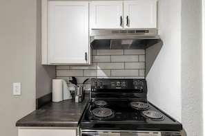 Une cuisine avec des meubles blancs, une cuisinière noire et un dosseret carrelé.