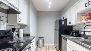 A compact kitchen with a stove, sink, and refrigerator, featuring white cabinets and a tiled backsplash. - Arlington 1BR | AT&T, Globe Life, 6 Flags, Parking (Arlington)