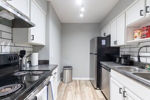 A compact kitchen with a stove, sink, and refrigerator, featuring white cabinets and a tiled backsplash. - Arlington 1BR | AT&T, Globe Life, 6 Flags, Parking (Arlington)