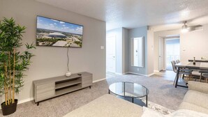 A living room with a flat-screen TV, a glass coffee table, a dining area with a table and chairs, and a potted plant. - Arlington 1BR | AT&T, Globe Life, 6 Flags, Parking (Arlington)