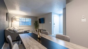 A modern meeting room with a long table, comfortable seating, a flat-screen TV, and a door. - Arlington 1BR | AT&T, Globe Life, 6 Flags, Parking (Arlington)