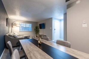 A modern meeting room with a long table, comfortable seating, a flat-screen TV, and a door. - Arlington 1BR | AT&T, Globe Life, 6 Flags, Parking (Arlington)