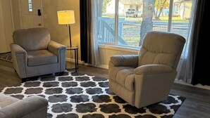 Una sala de estar con dos sillones, una lámpara y un tapete estampado.