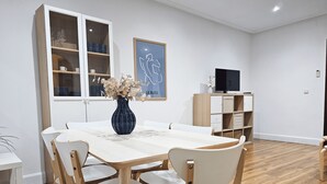 Ein moderner Essbereich mit einem Holztisch, Stühlen, einer Vase mit Blumen und einem Fernseher auf einem Schrank.